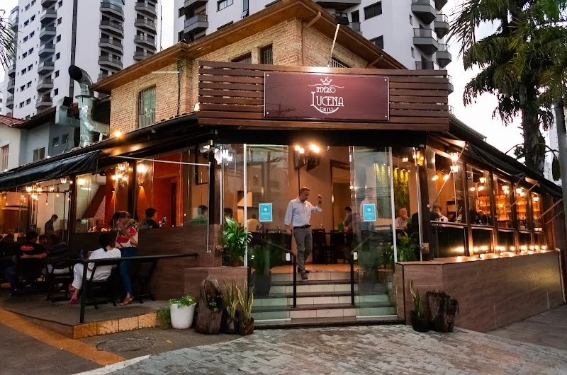 Fachada do Império Lucena Grill à noite, com varanda iluminada e mesas na calçada